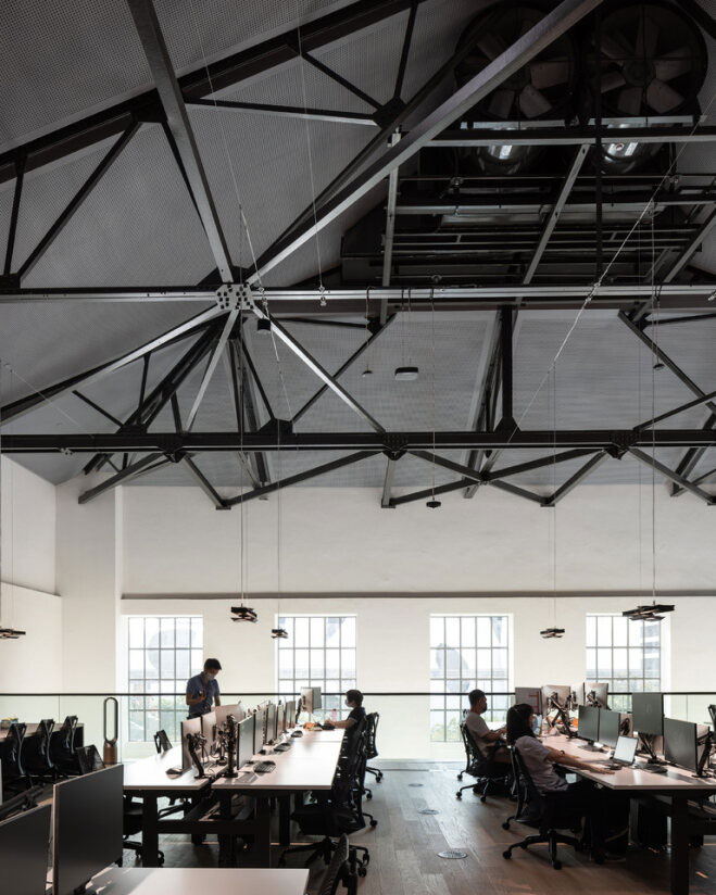 An example of adaptive reuse, this office workspace features an open-plan design under a retrofitted industrial ceiling with original trusses.